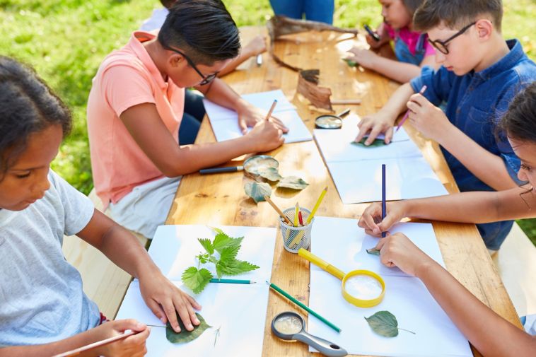 Auch im Jahr 2026 wieder: Kinder basteln und malen gemeinsam am Tisch im Rahmen des Regionalen Ferienpasses. Foto: Adobe Stock